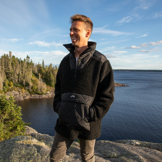 Homme souriant, installé sur un cap de roche avec vue sur la mer un jour d'automne