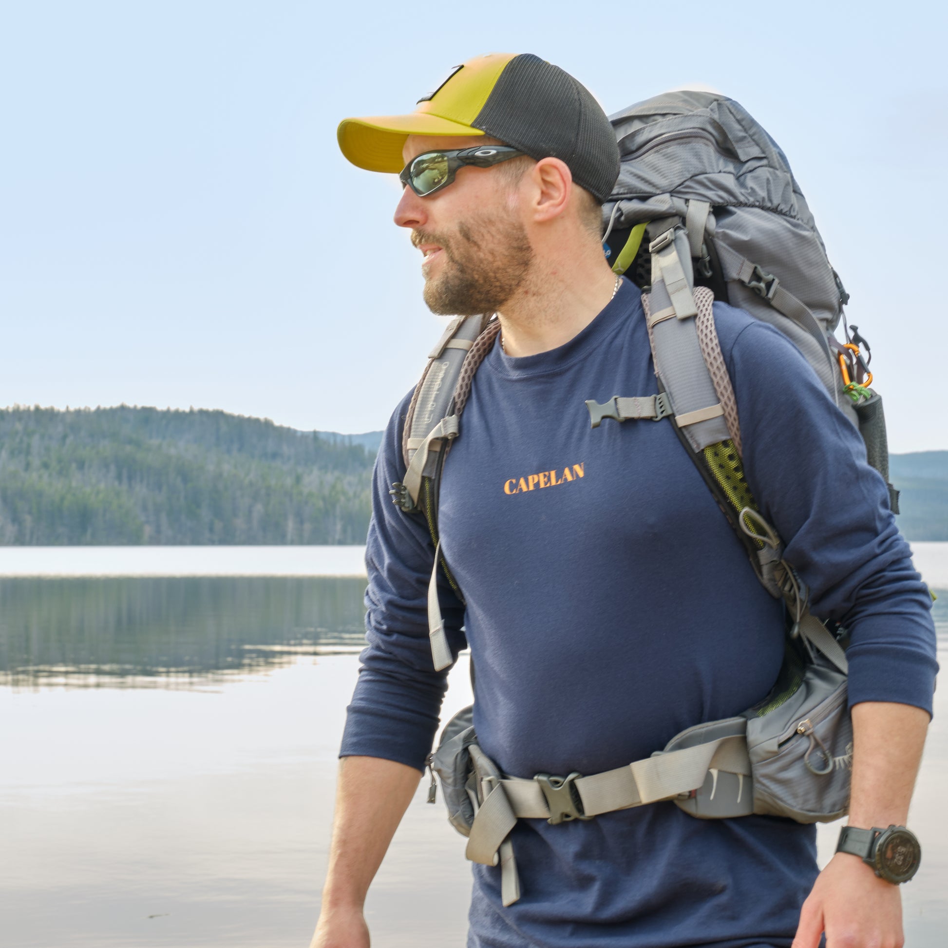 Homme qui porte un sac, près à parti à l'aventure installé près d'un lac entouré de conifères