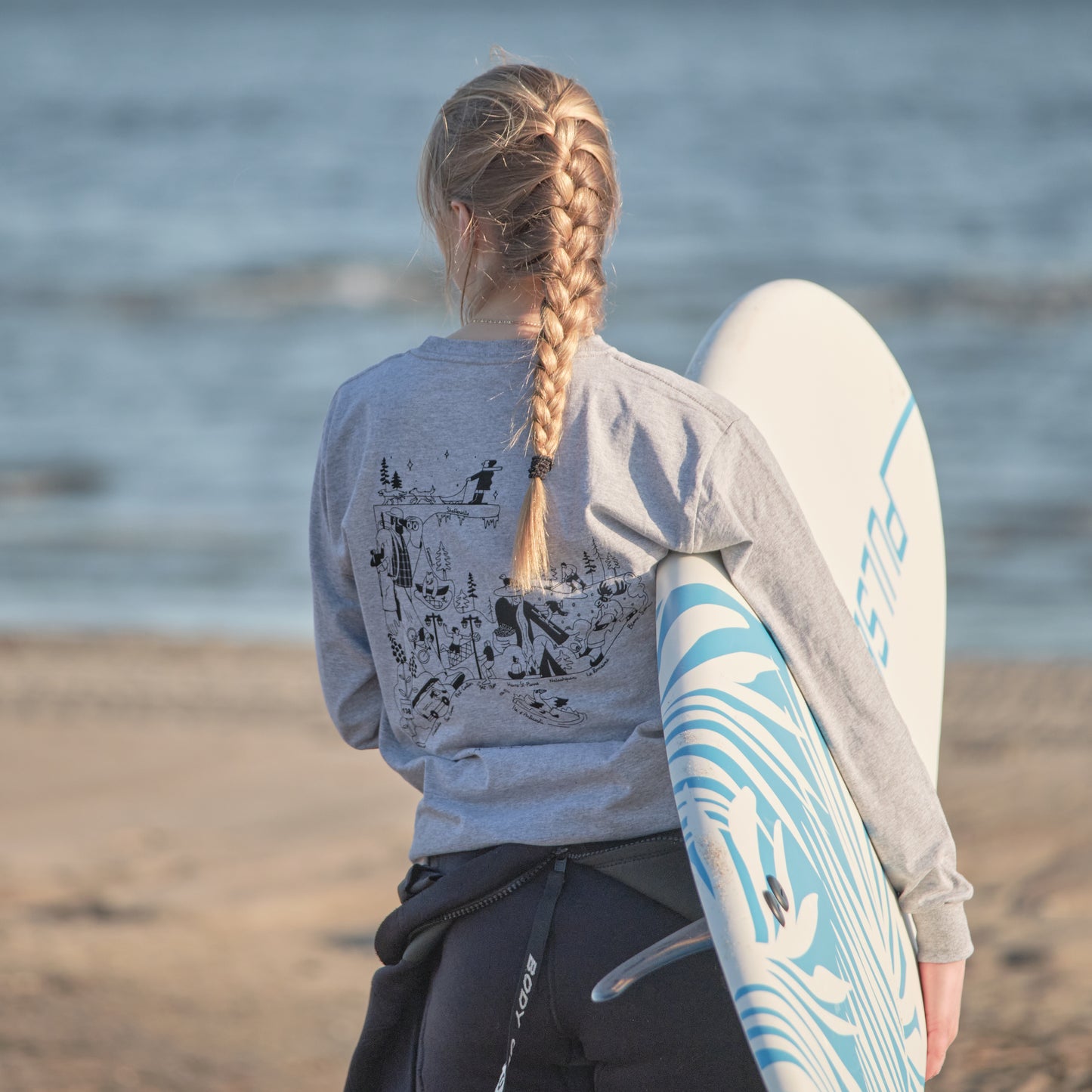 Femme avec un surf sous le bras portant le t-shirts manches longues Plein air regardant la mer